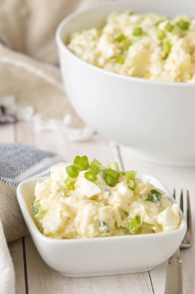 potato salad in serving dish with large bowl of potato salad in background