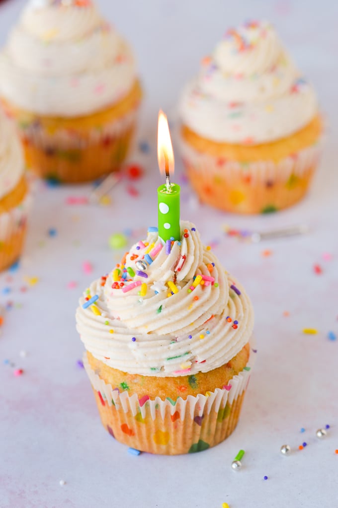 cake batter frosting on cupcake with sprinkles and lit candle 