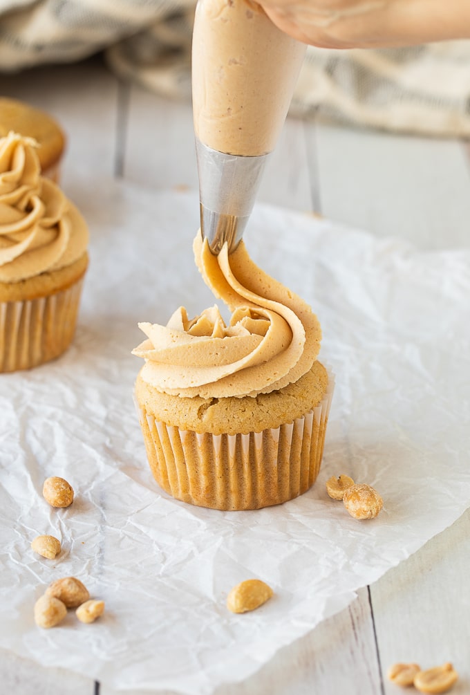 close up piping peanut butter frosting on cupcake