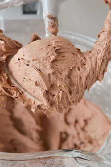 chocolate buttercream on standing mixer beater attached to mixer above the bowl.