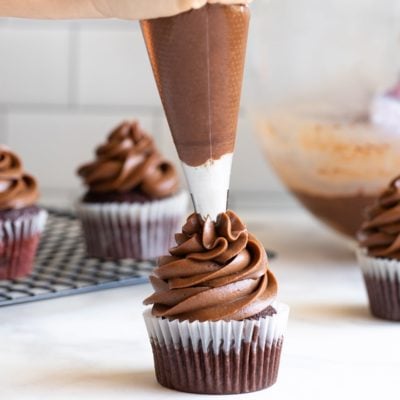 piping chocolate cream cheese frosting on cupcake