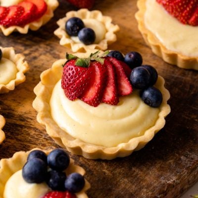 mini fruit tarts with strawberries and blueberry on wood board.
