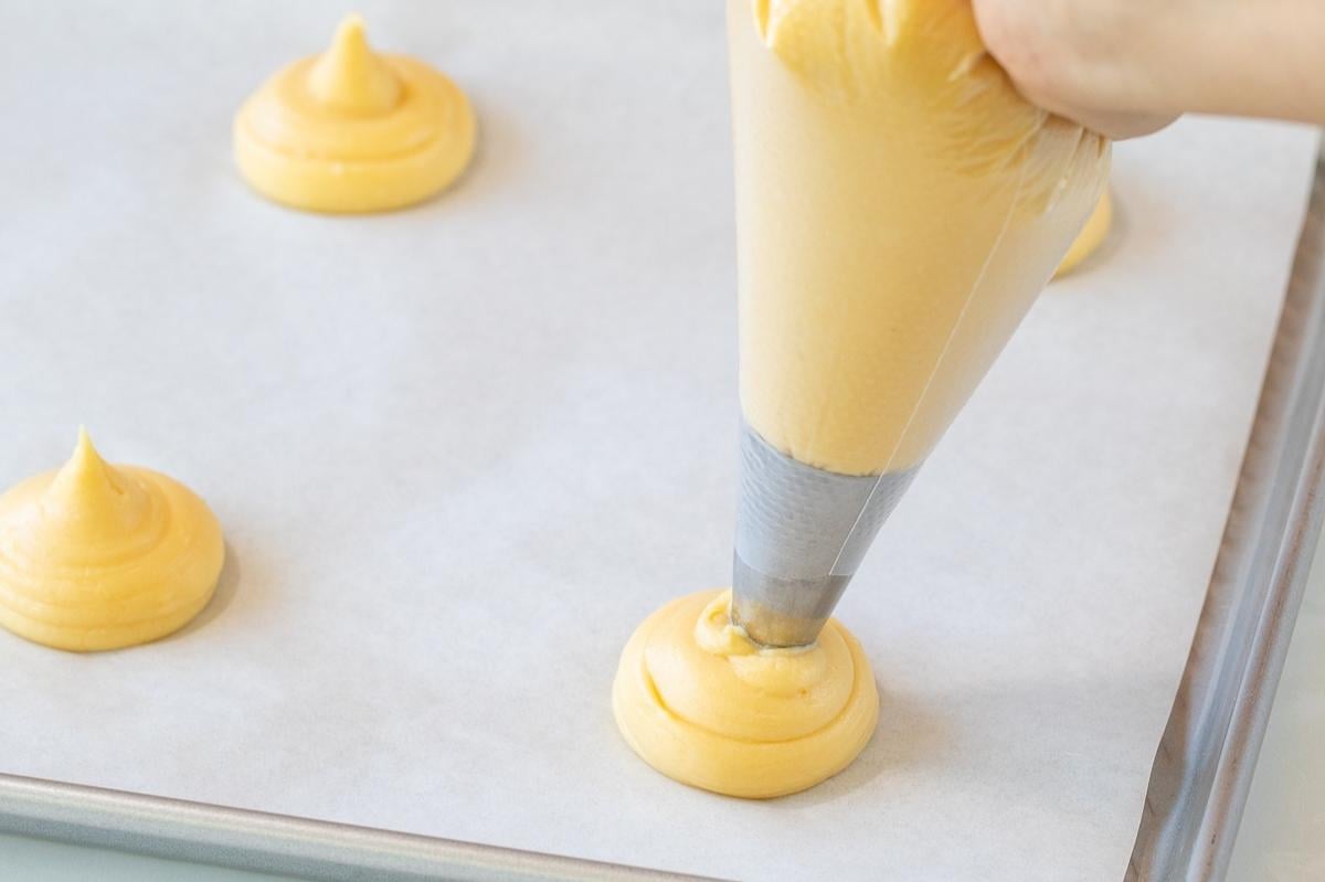 piping choux pastry onto baking sheet for cream puffs.