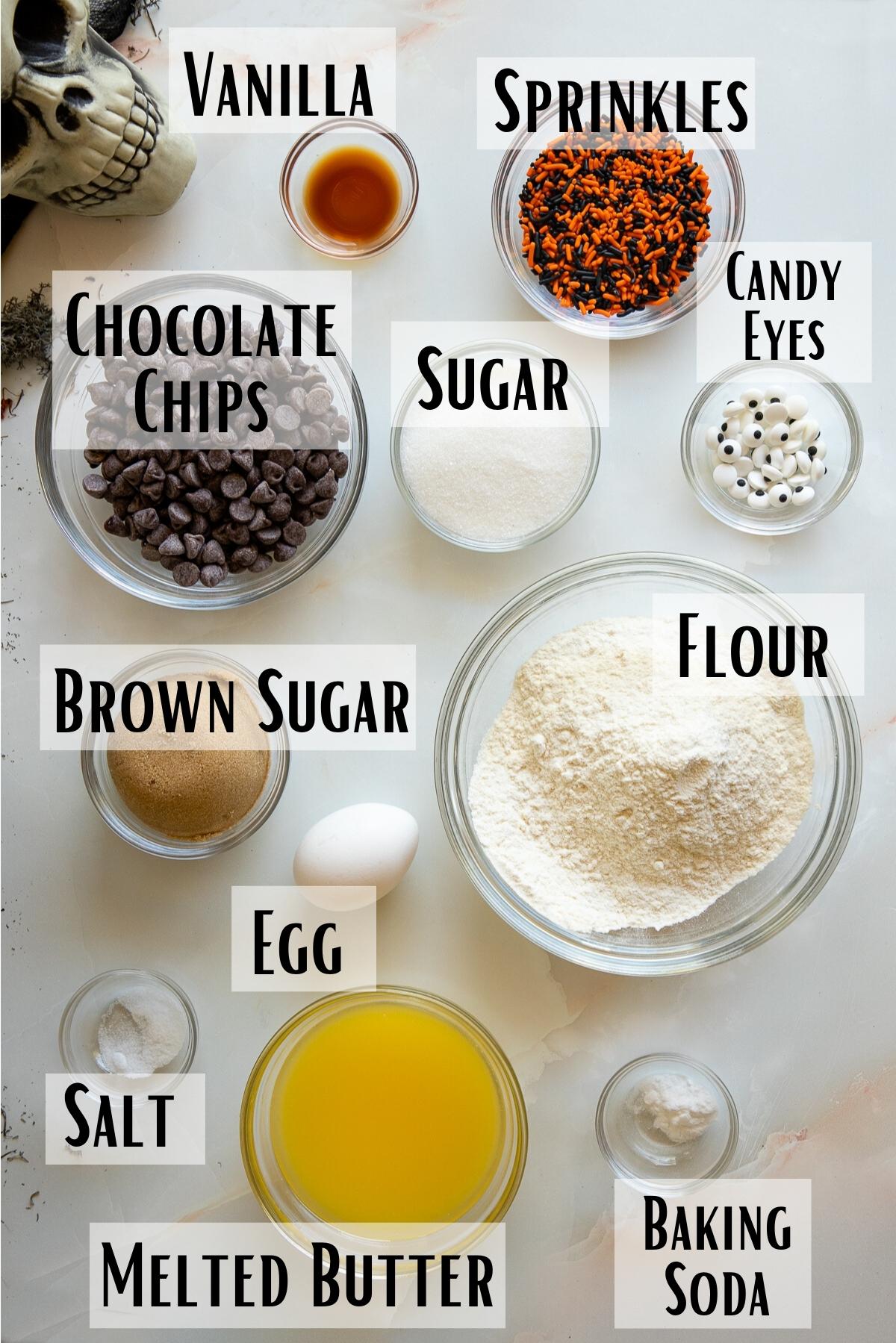 Halloween chocolate chip cookie ingredients of all purpose flour, granulated sugar, brown sugar, vanilla, egg, salt, baking soda, chocolate chips, sprinkles and candy eyes. 