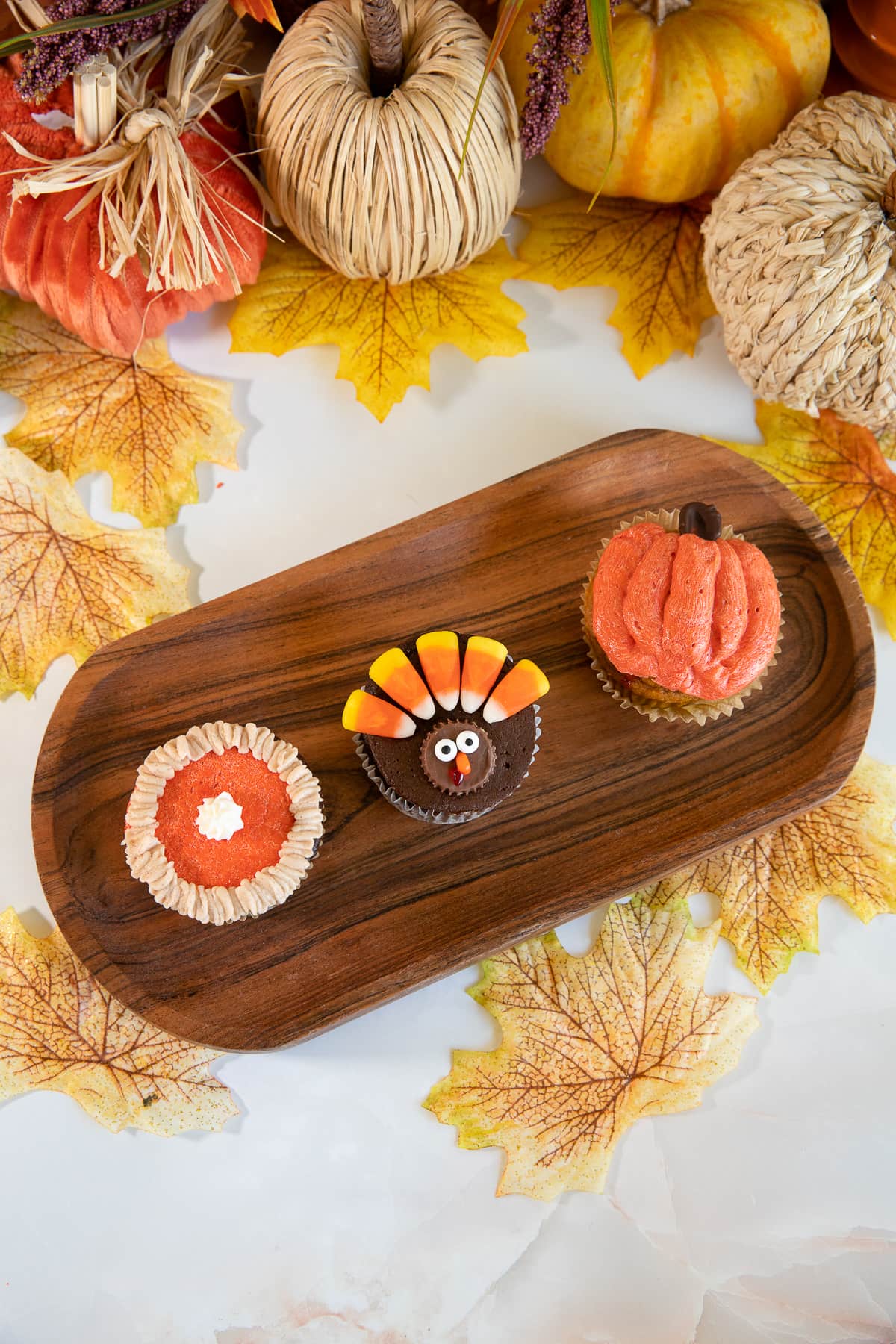 turkey, pie, and pumpkin decorated cupcakes on wooden tray.