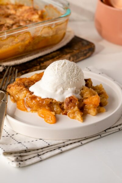 baked peach cobbler with cake mix on serving plate with ice cream.