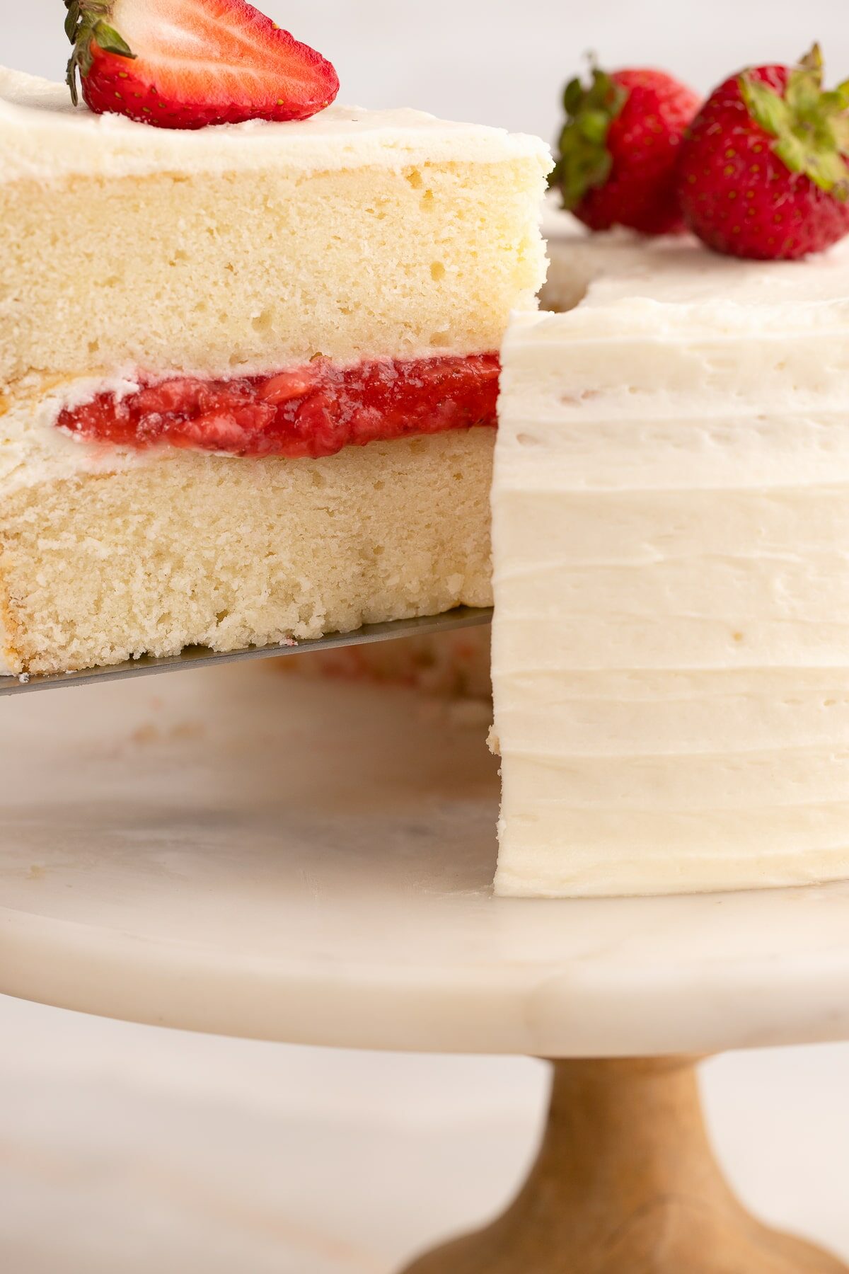 slicing a vanilla cake with strawberry filling up close.