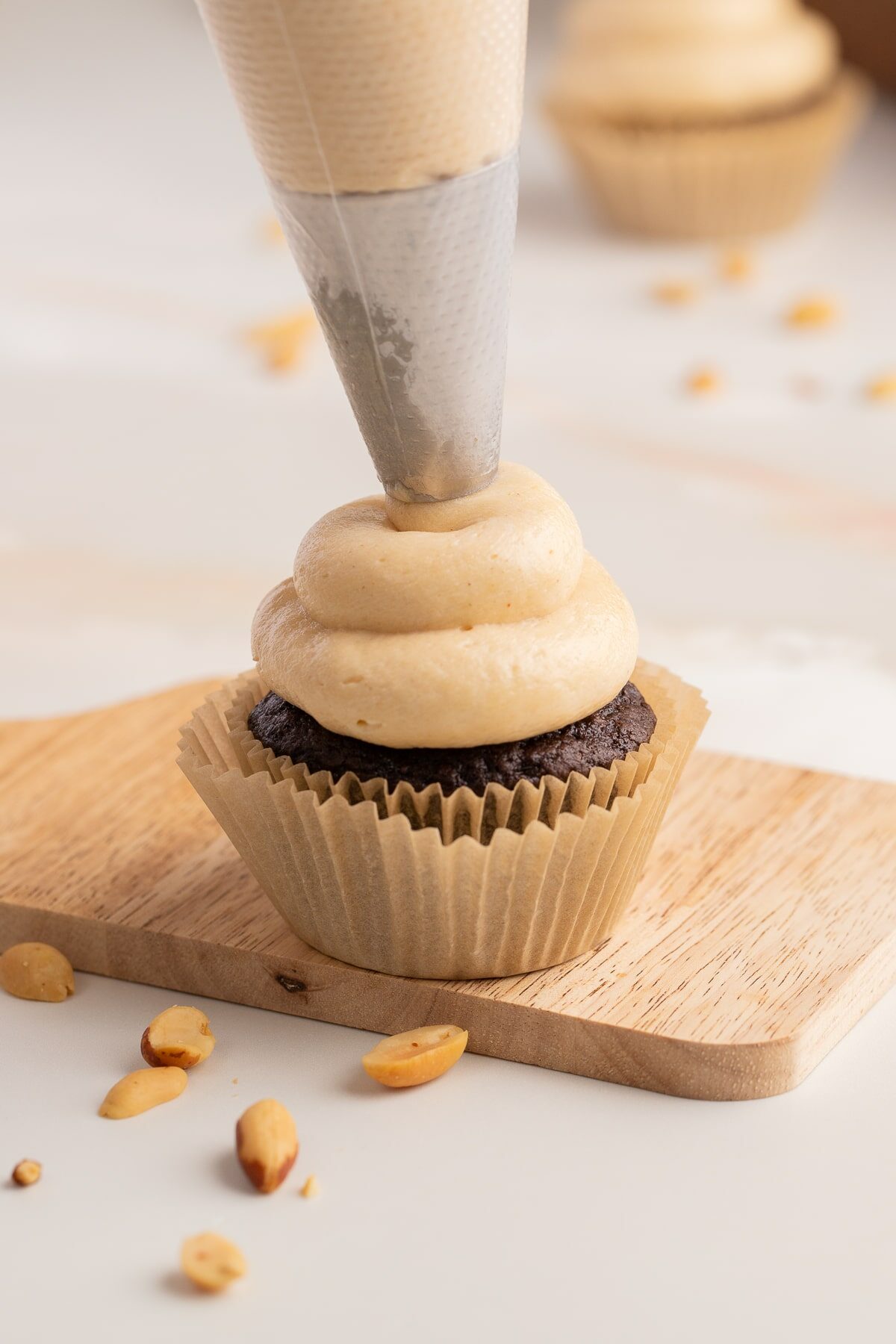 piping peanut butter cream cheese frosting on chocolate cupcake.