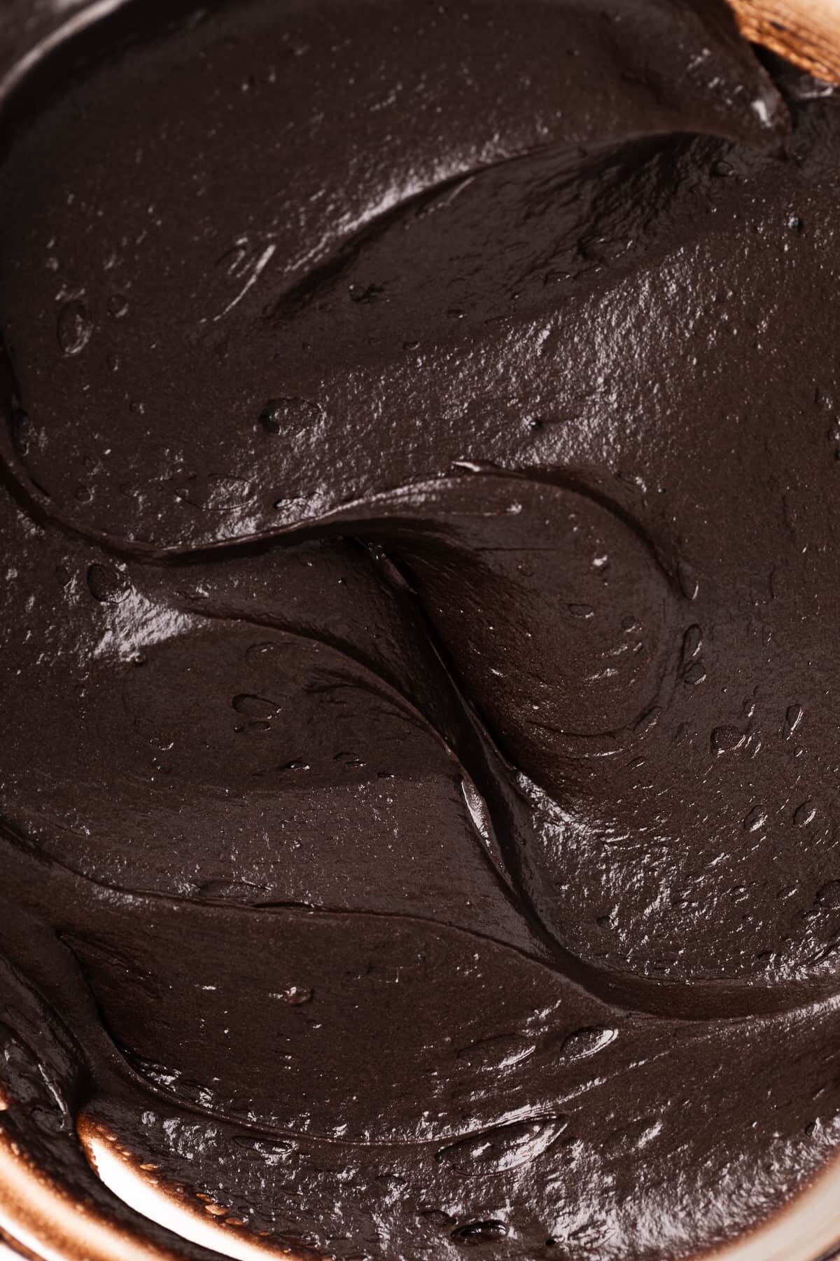 black cream cheese frosting swirled in mixing bowl up close.