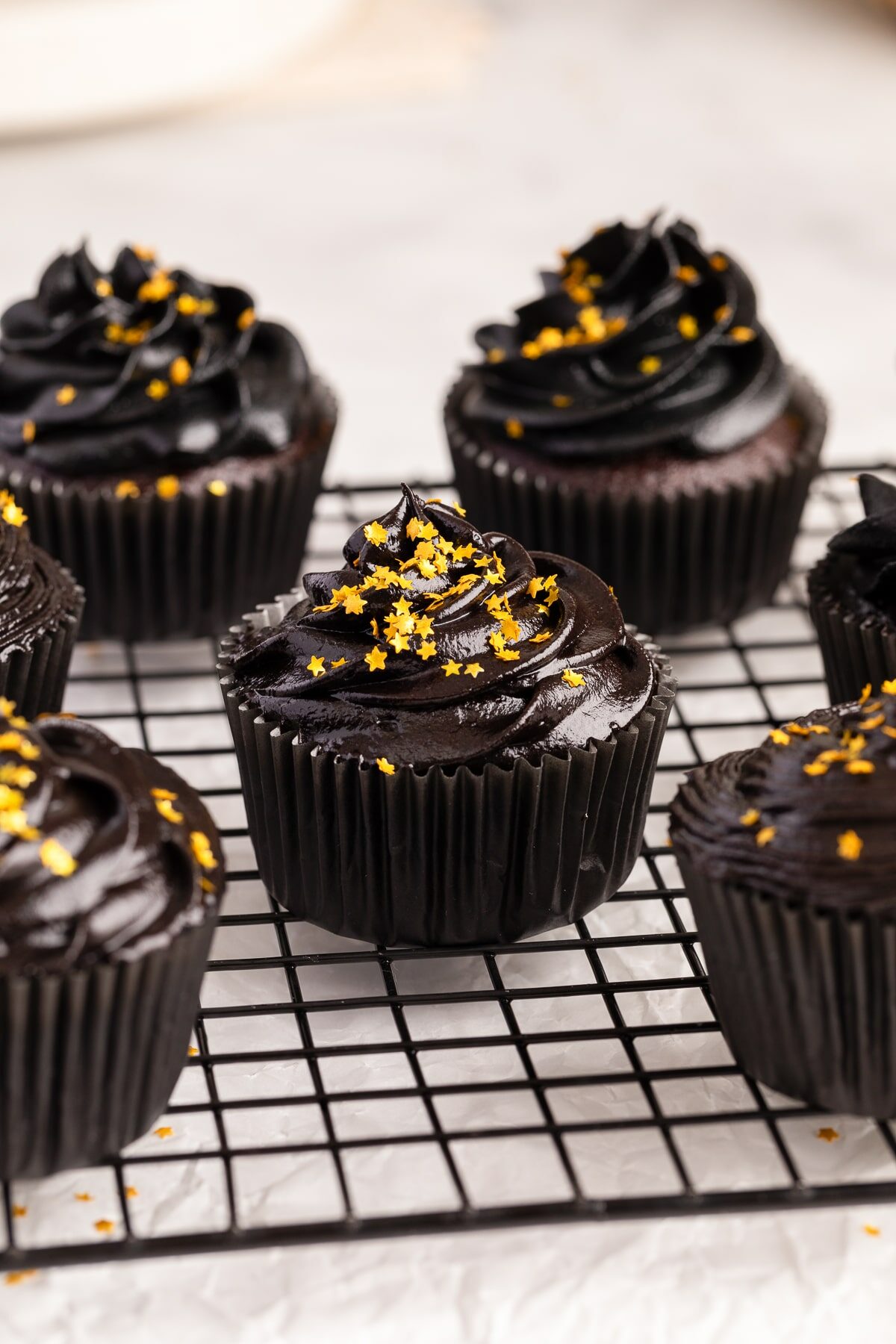 chocolate cupcake with black cream cheese frosting frosting and gold sprinkles on cooling rack.