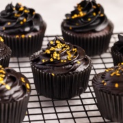 chocolate cupcake with black cream cheese frosting frosting and gold sprinkles on cooling rack.