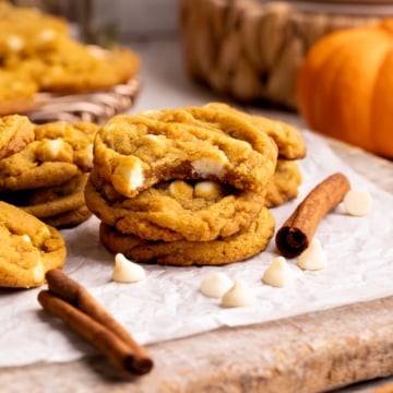 pumpkin white chocolate chip cookies stacked with bite taken out.