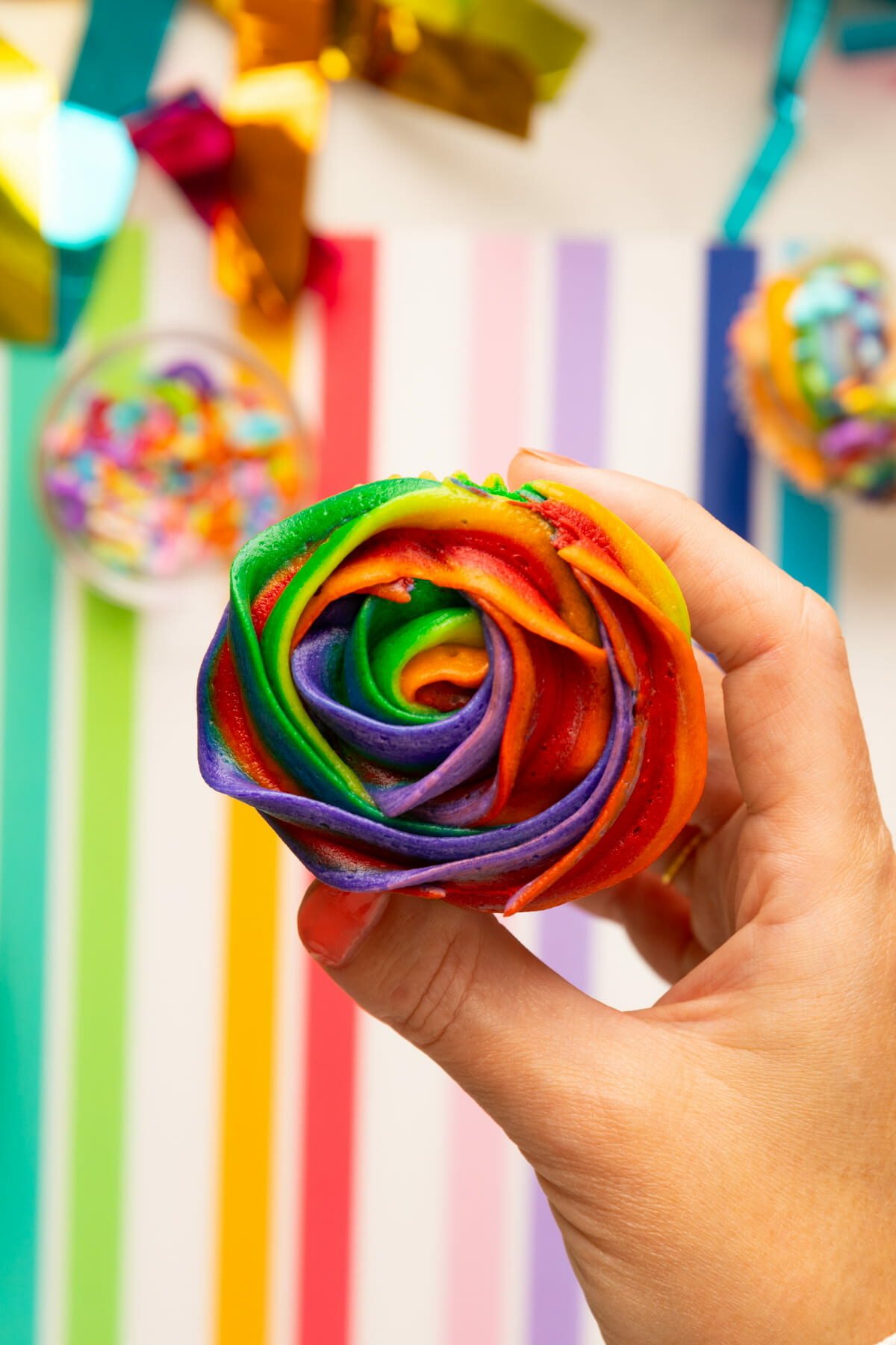 holding cupcake with rainbow frosting on top.