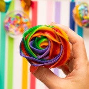 holding cupcake with rainbow frosting on top.