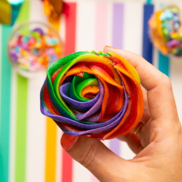 holding cupcake with rainbow frosting on top.
