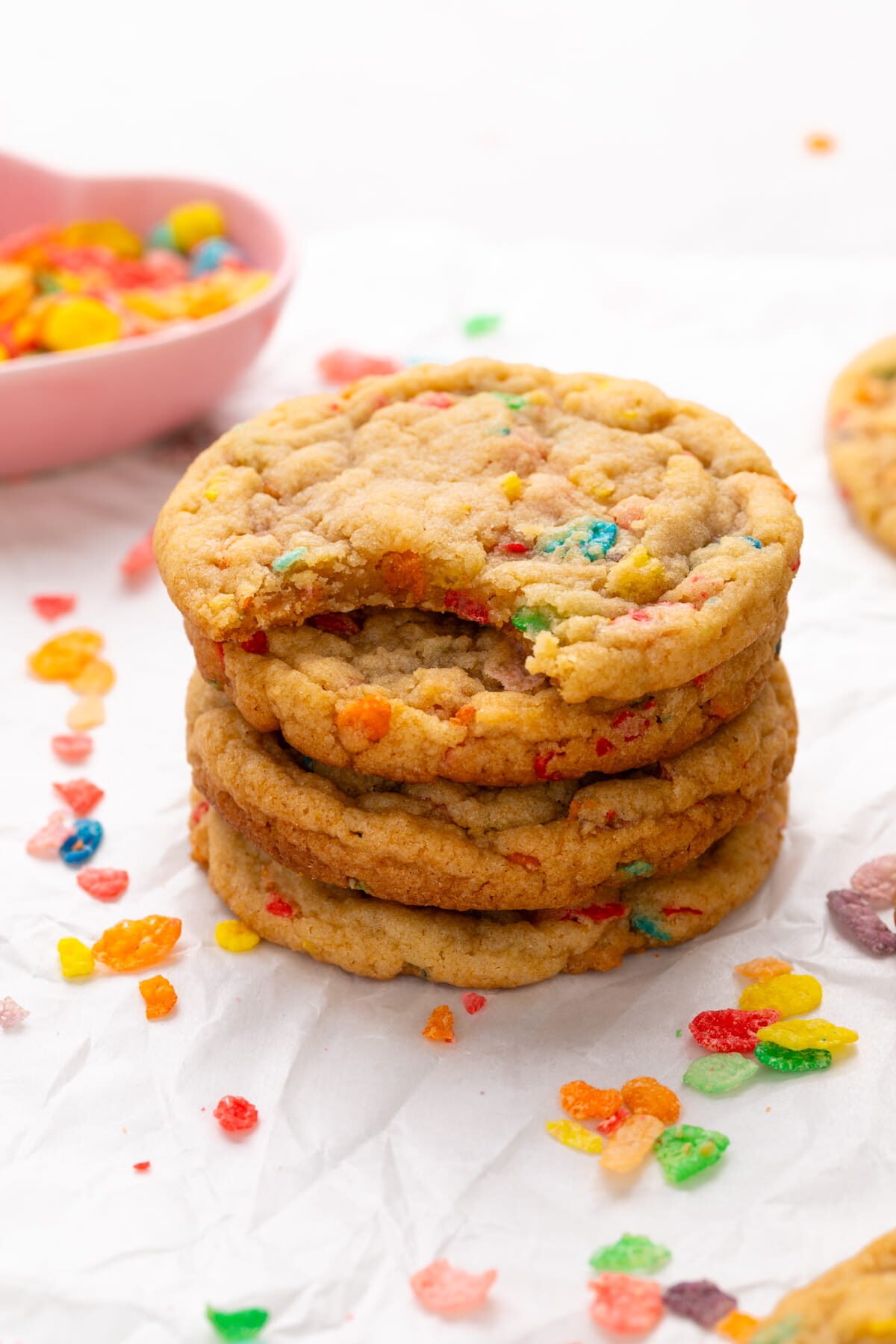 fruity pebble cookies stacked on parchment with a bite taken out of one.