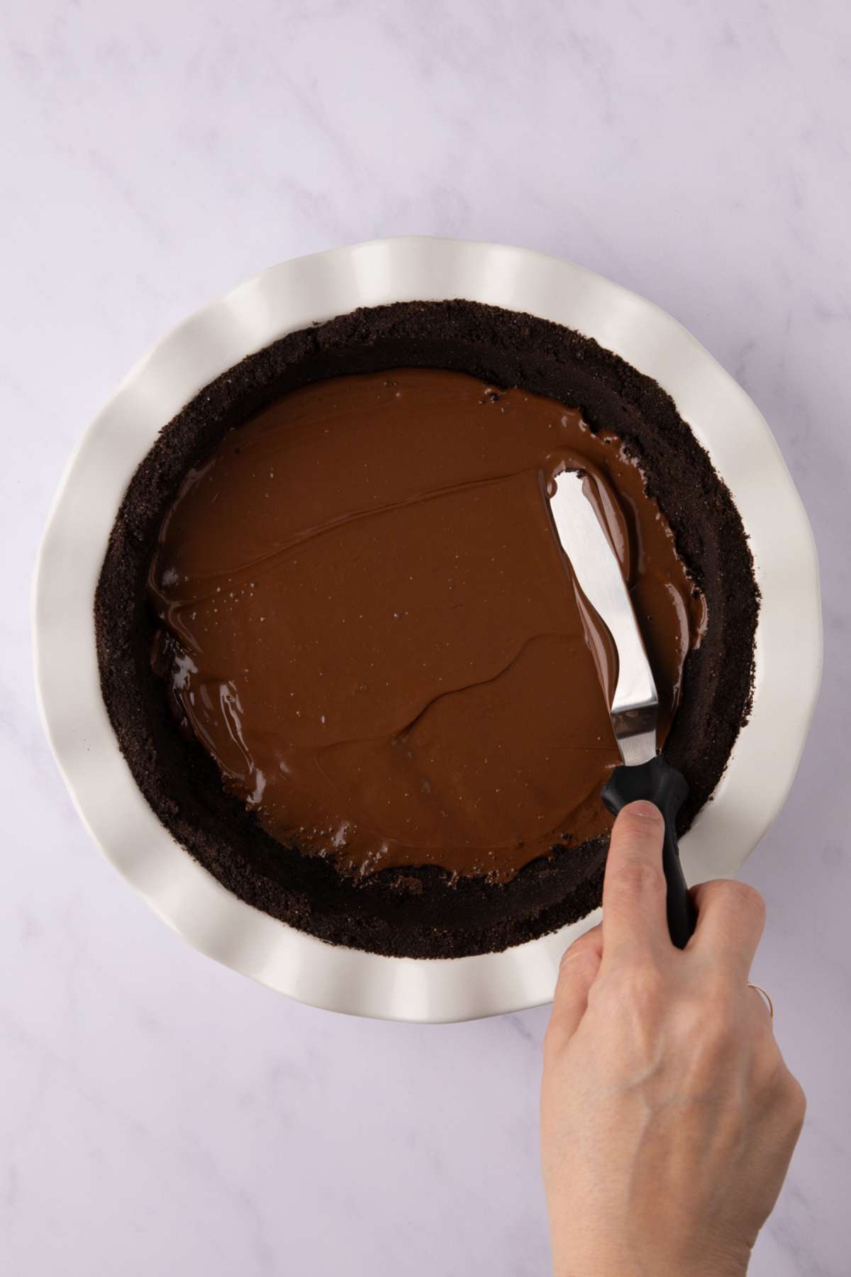 spreading nutella on the bottom of an oreo crust in a white pie pan.