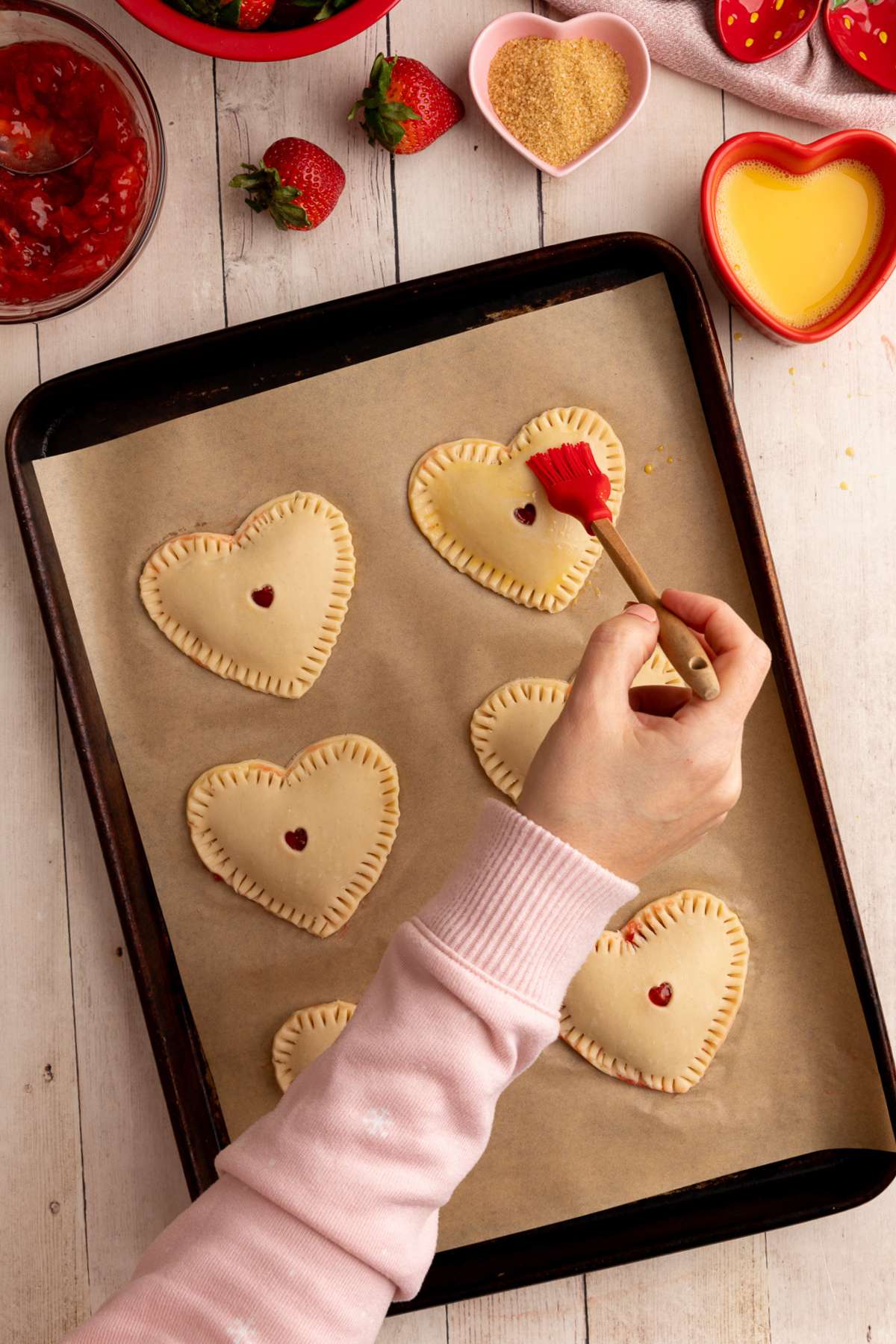 6 filled and closed hand pies on a parchment lined baking sheet, and adding an egg wash to the top of the pies.