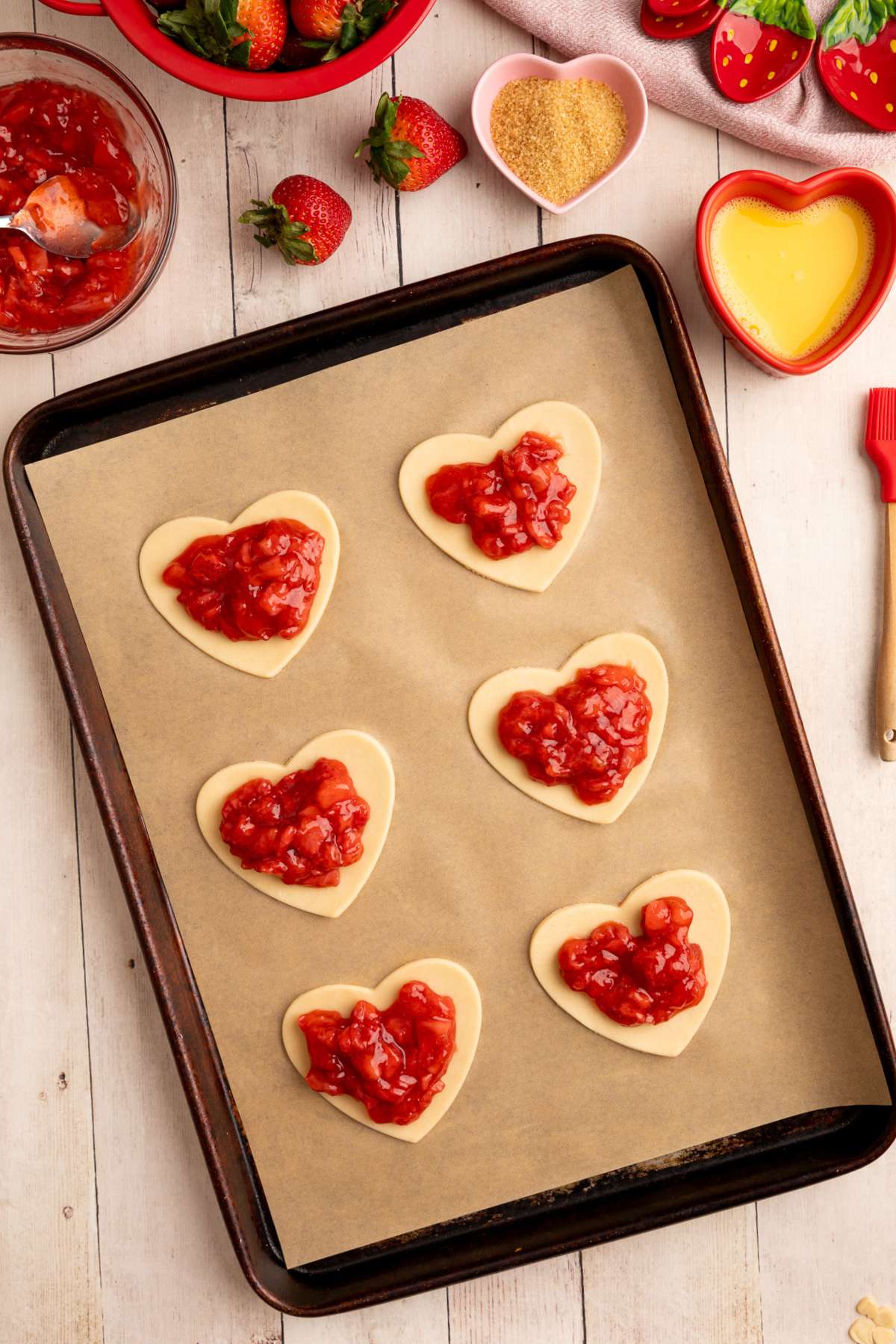 6 heat shaped unbaked pie crust on a parchment lined baking sheet with a tablespoon or so of filling in the middle of each crust.