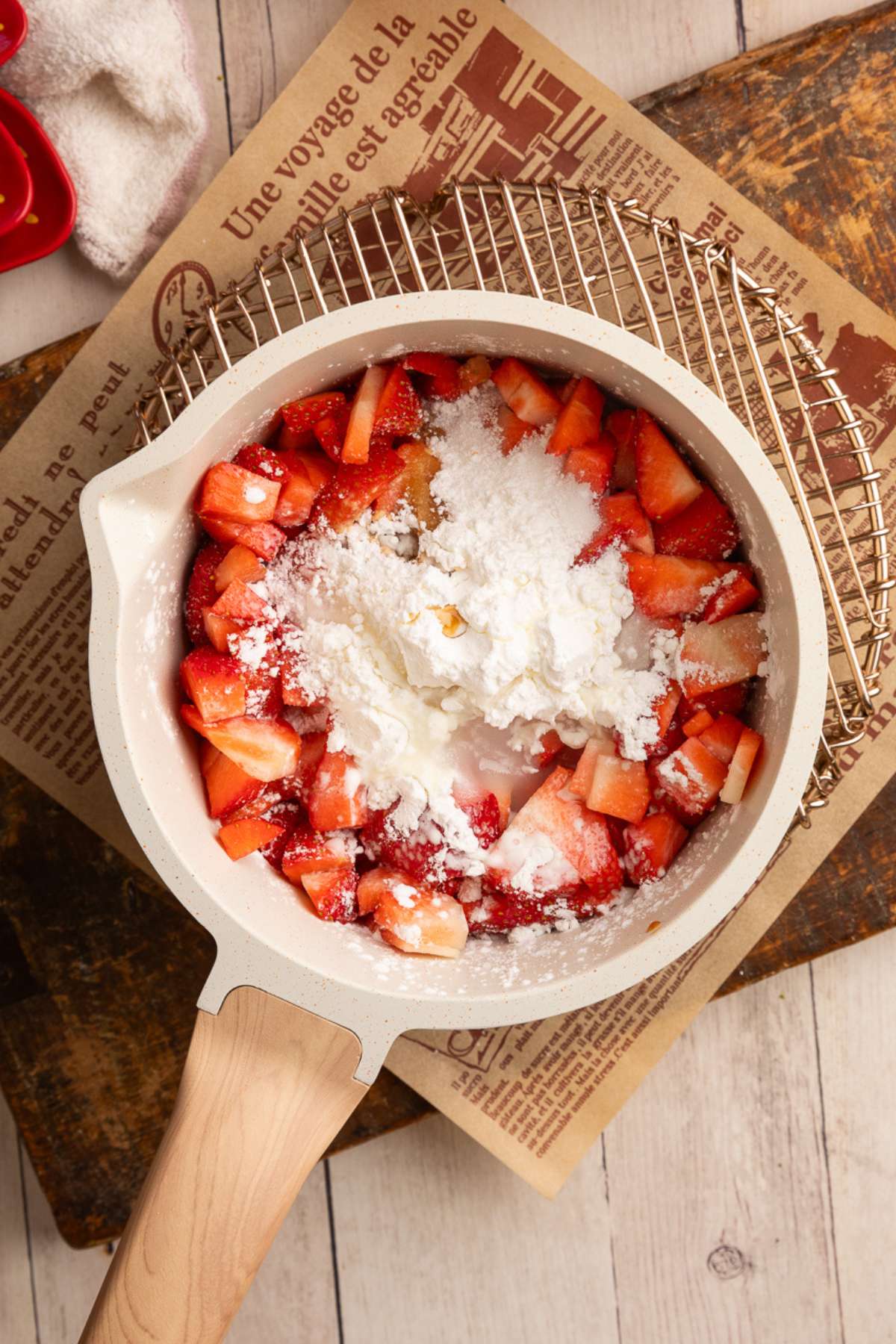 unmixed strawberry filling ingredients in a cream colored saucepan on metal rack.