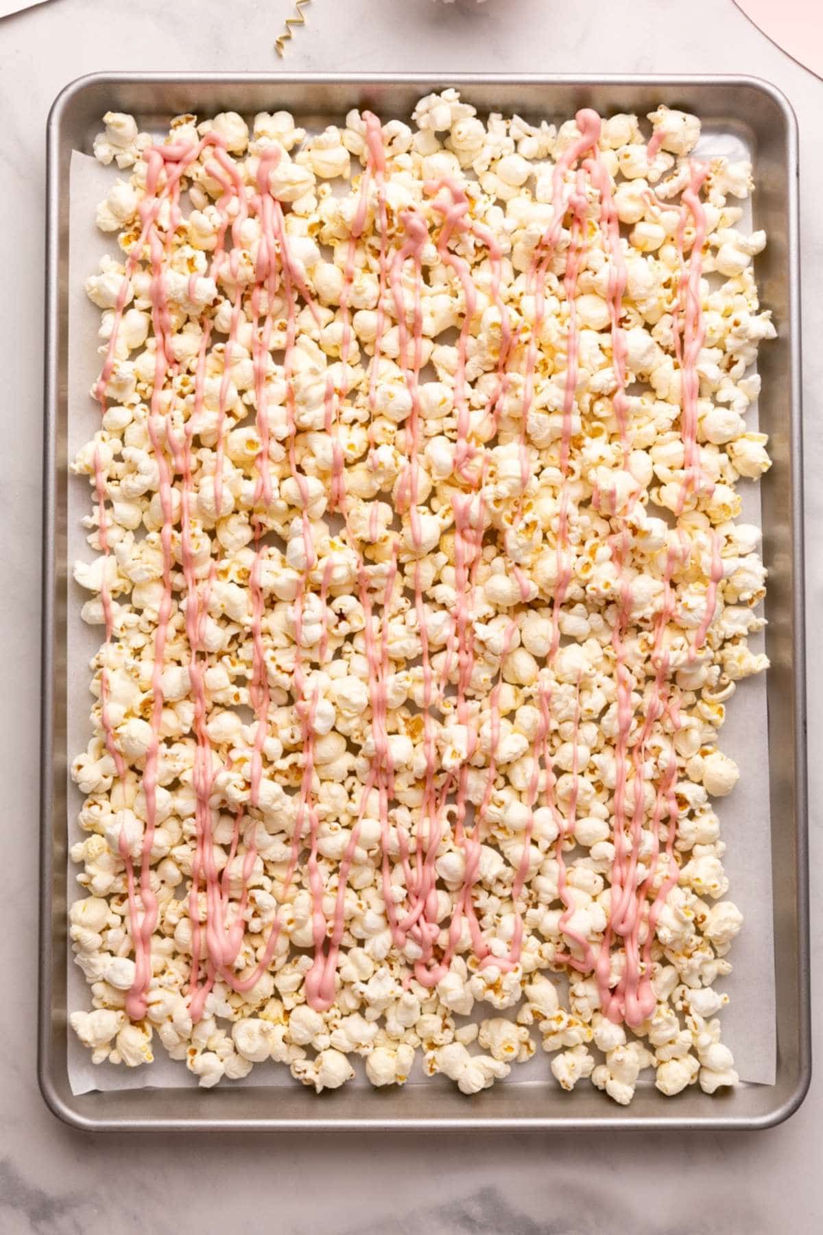 valentine's day popcorn on a baking sheet, topped with melted pink chocolate.
