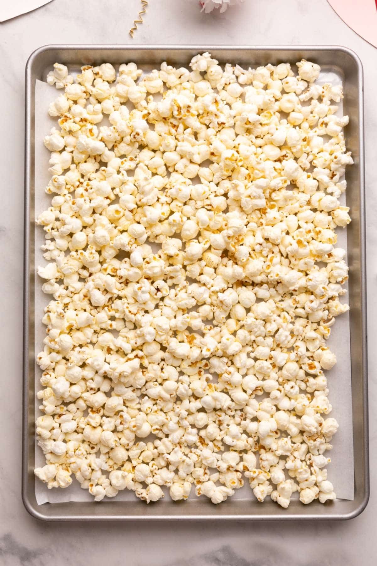 plain popcorn on a single layer on a parchment lined baking sheet.