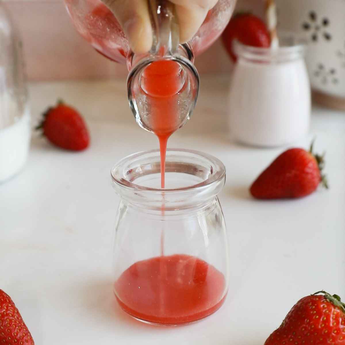 pouring strawberry syrup into a small glass milk bottle.
