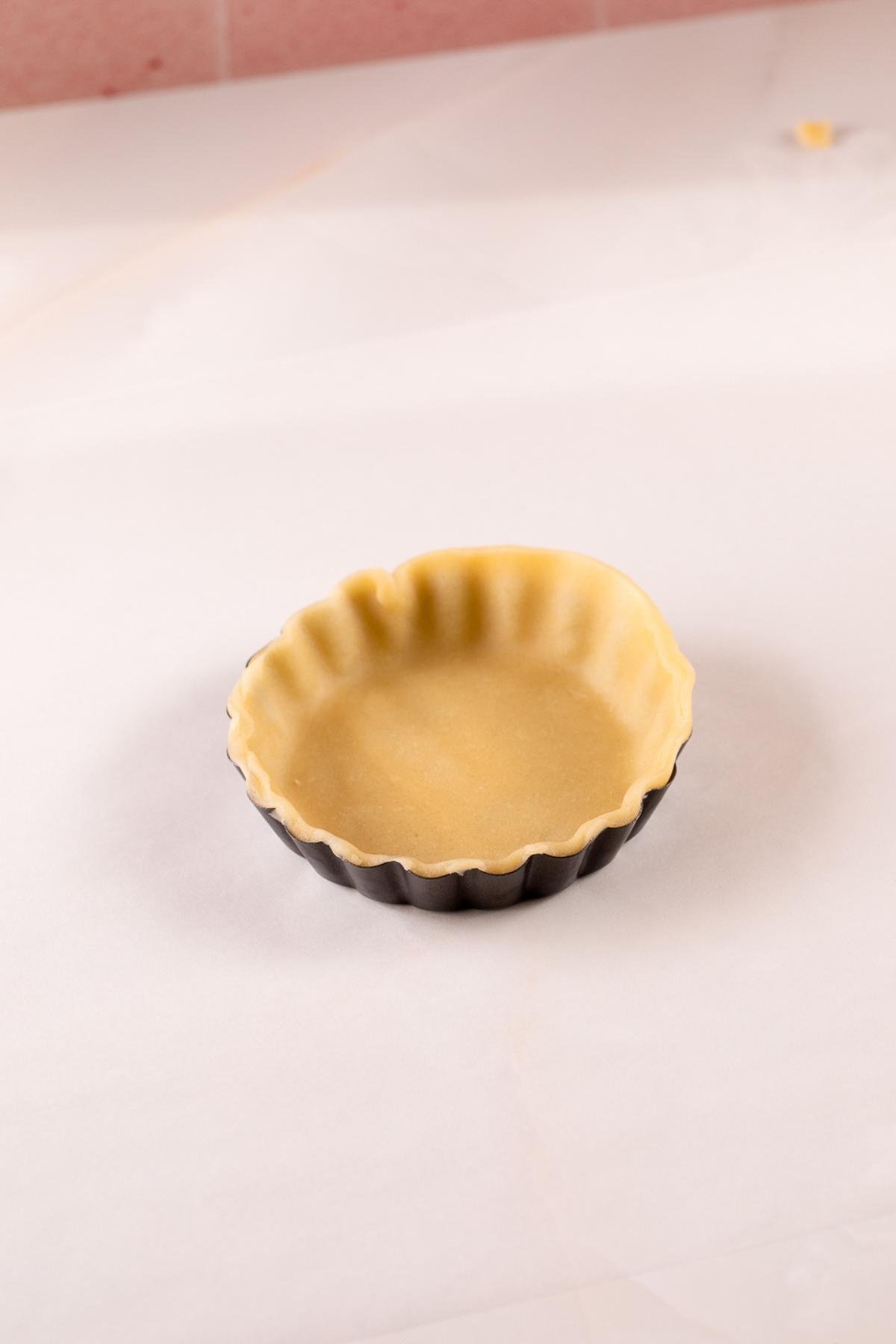unbaked tart dough in a 4 inch tart pan, with an edge than needs to be trimmed.