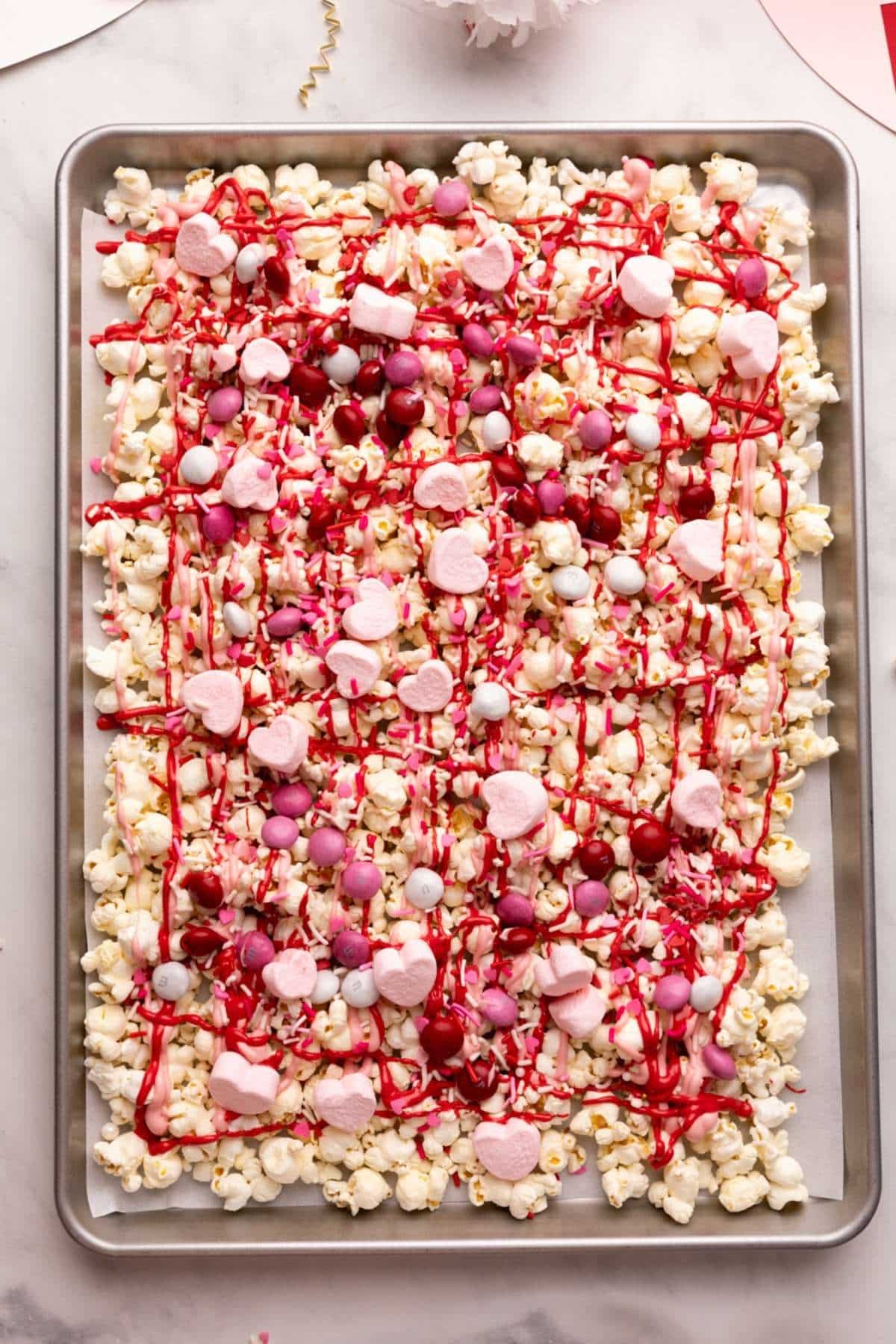 valentine's day popcorn on a baking sheet, topped with melted chocolate and toppings.