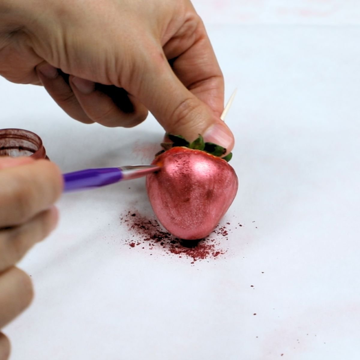 painting dark pink edible luster dust on a dried pink chocolate covered strawberry. .