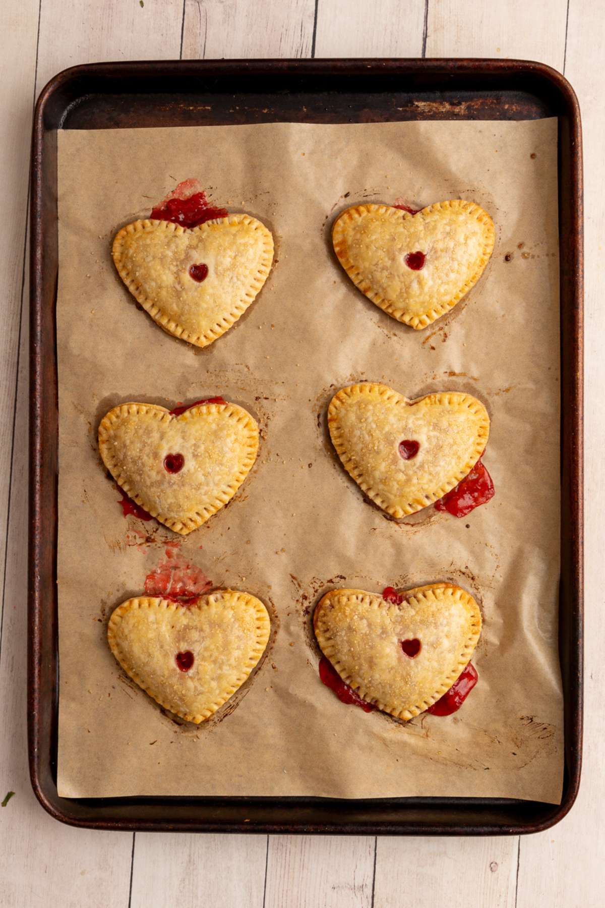 golden brown baked heart shaped hand pies on a baking sheet lined with brown parchment paper.