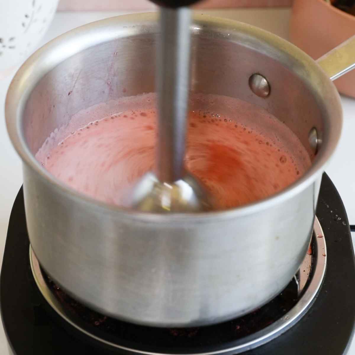 using an immersion blender on cooked swrawberry syrup in a metal pot.