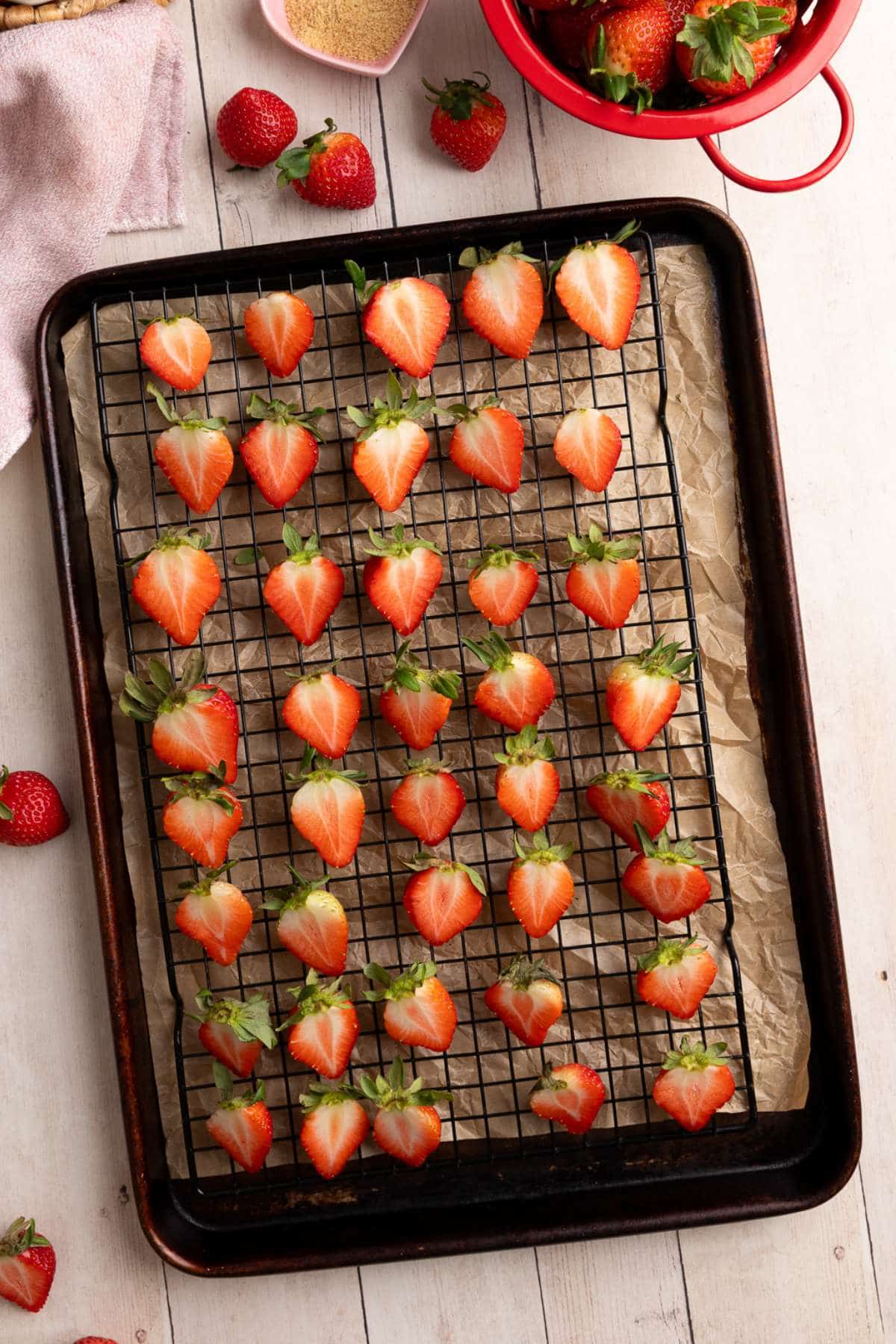 a cooling rack on top of a parchment lined baking sheet with halved strawberries on top.