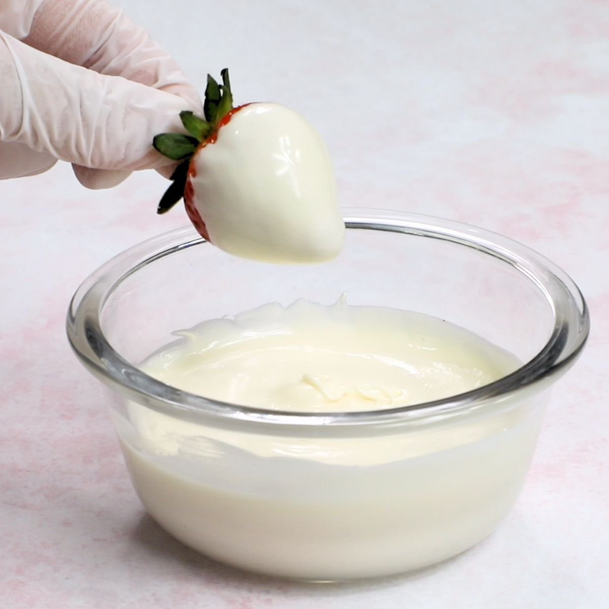 dipping a medium size strawberry in a bowl of melted white candy melts.
