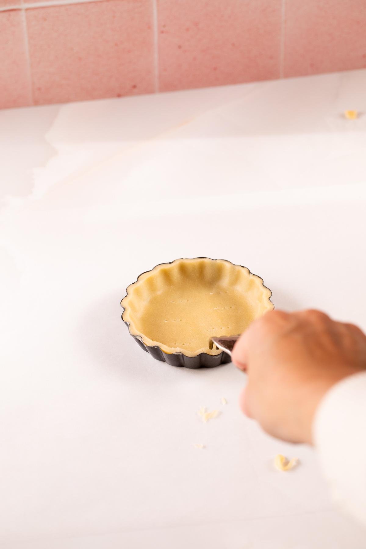 docking, or piercing unbaked mini tarts in a tart pan with a fork.