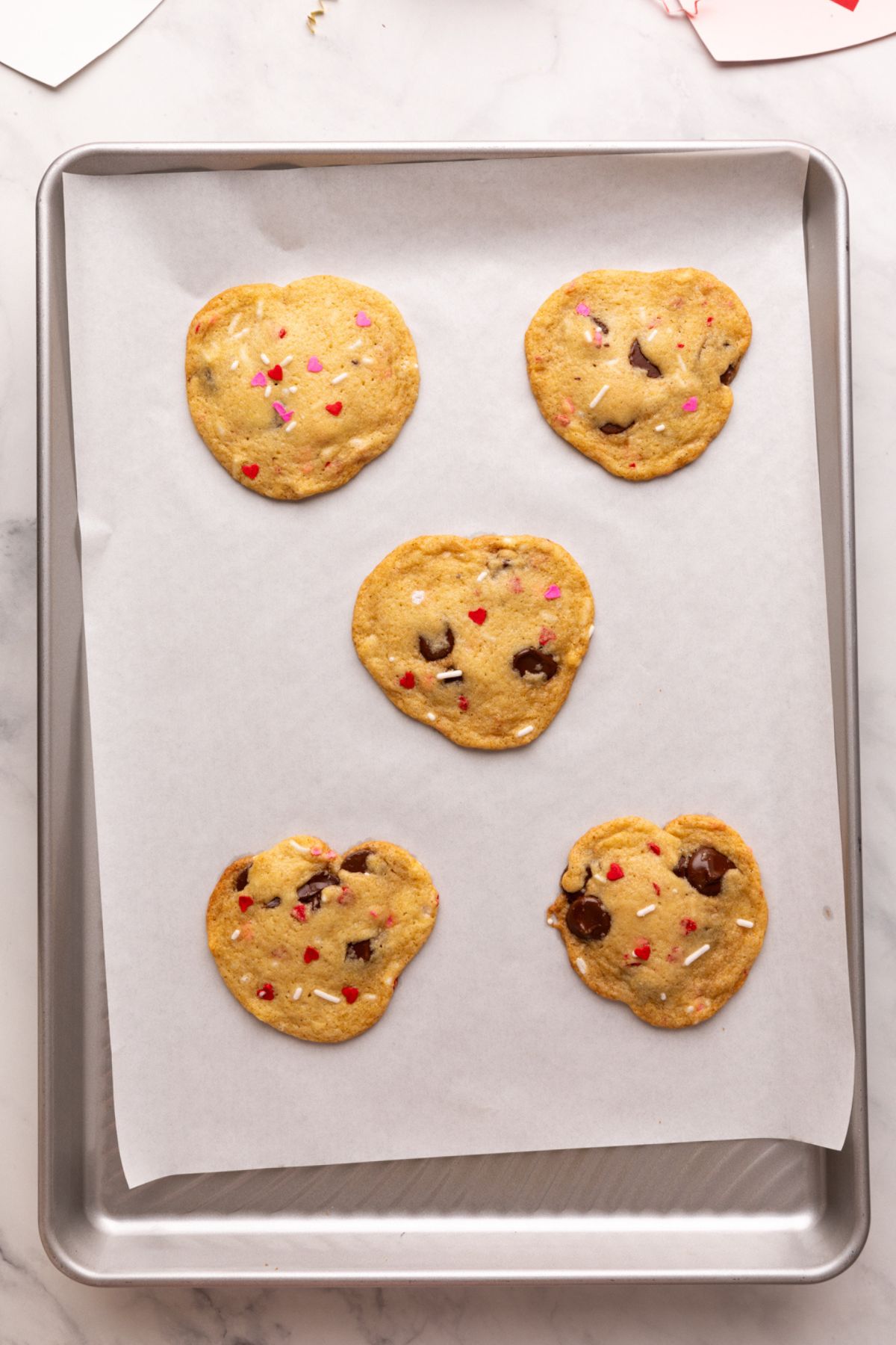 baked and unshaped heart chocolate chip cookies on baking sheet.
