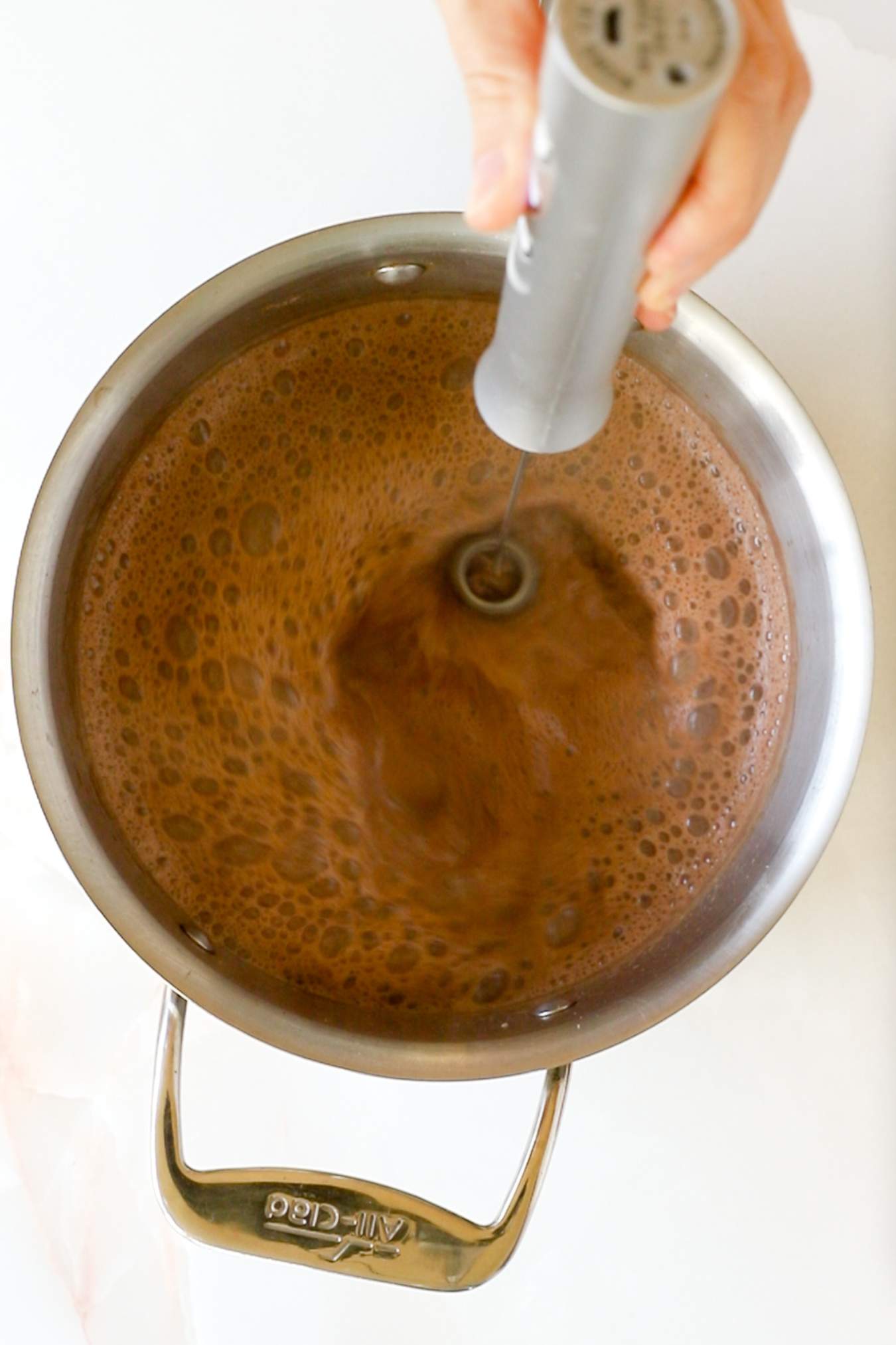 using a hand held milk frother on the hot chocolate in the saucepan.
