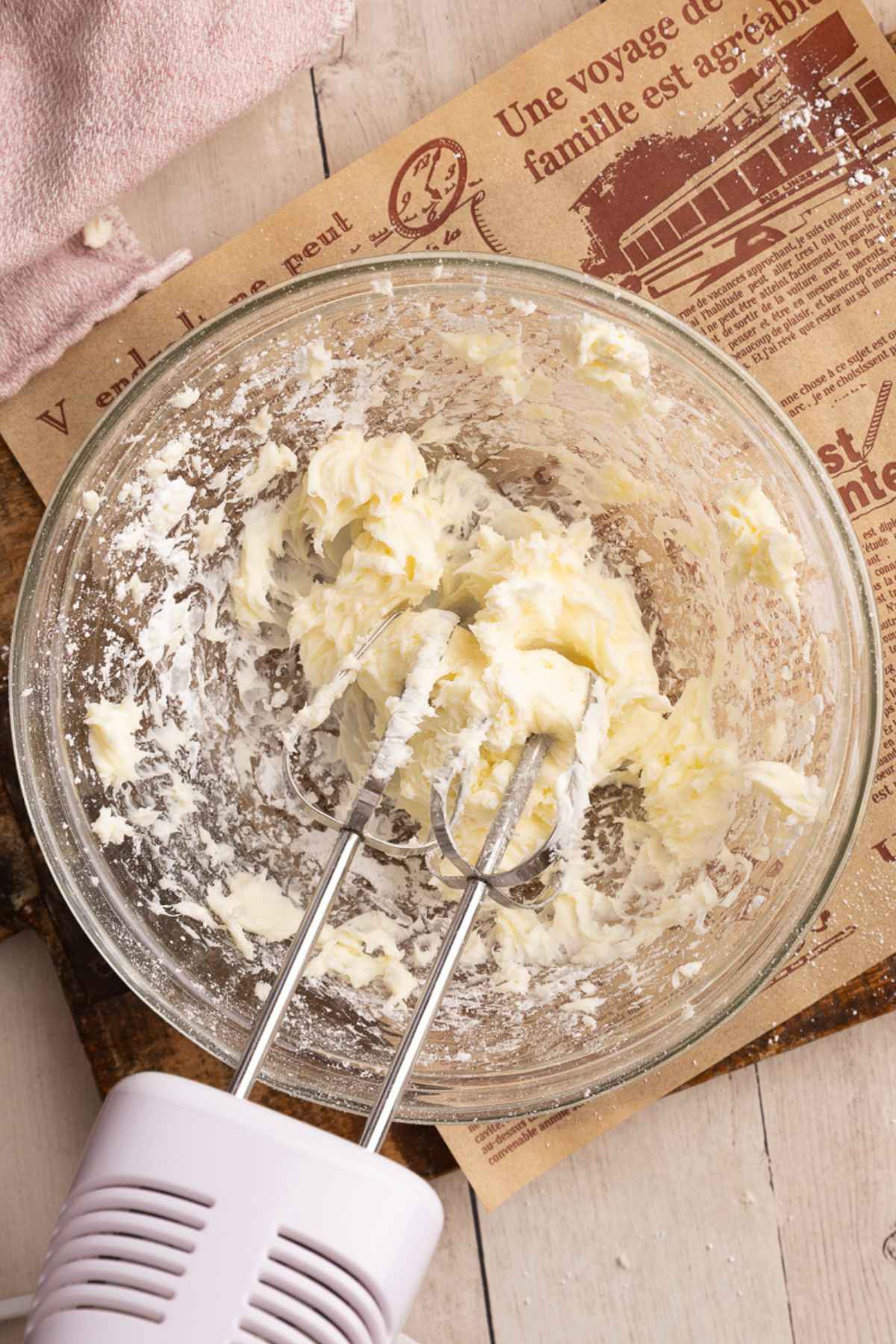 cream cheese and powdered sugar in a glass bowl with a hand held mixer.