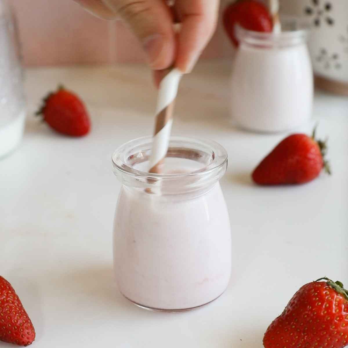 stirring milk and strawberry syrup in a glass bottle with a paper straw.