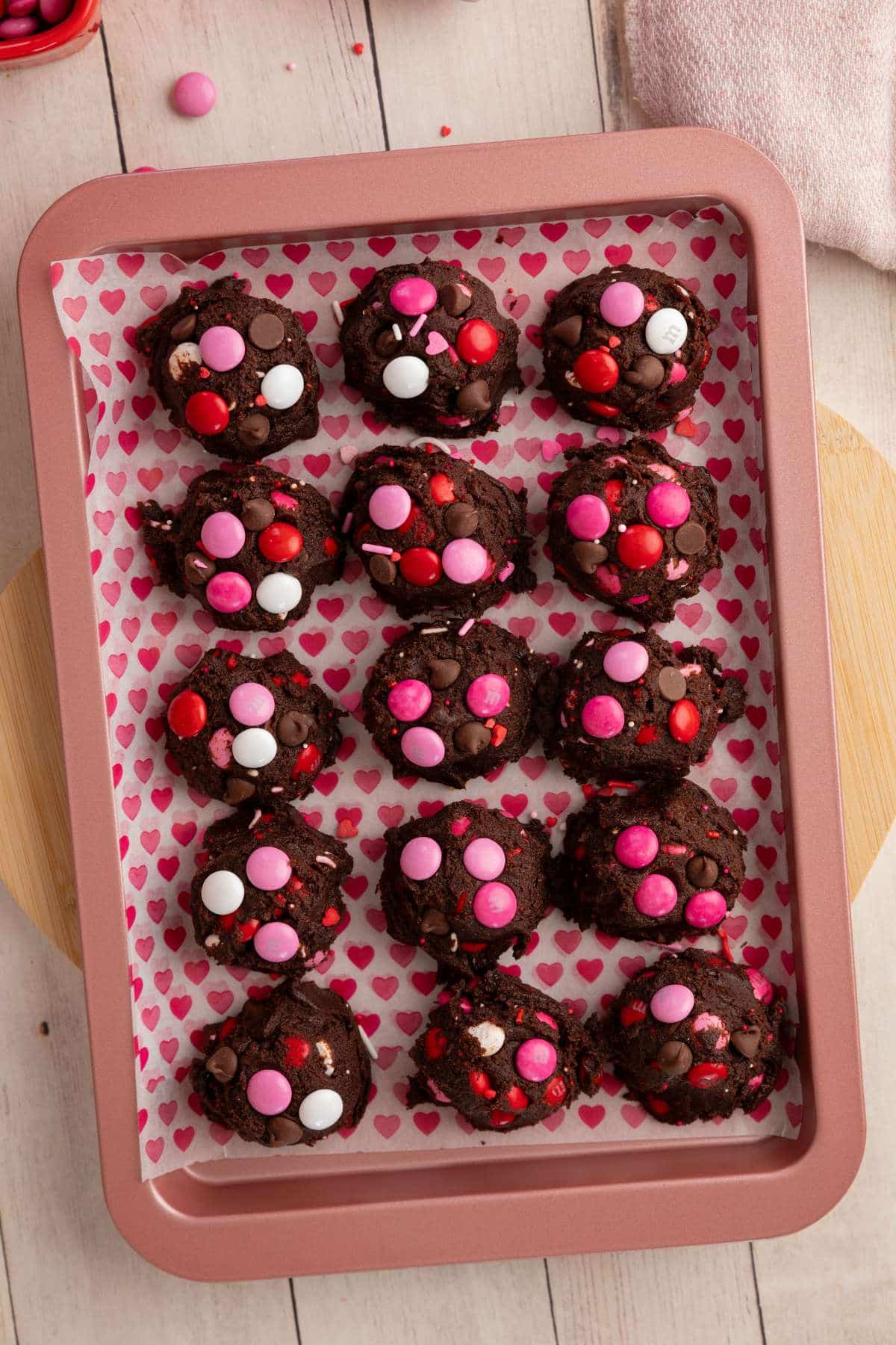 balls of cookie dough for chilling on a pink baking sheet lined with heart parchment paper.