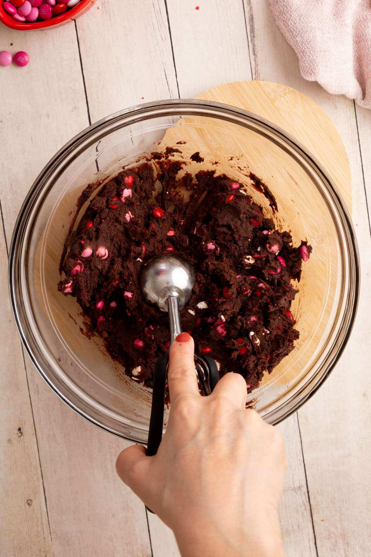 using an ice cream scoop to scoop cookie dough from a glass bowl.