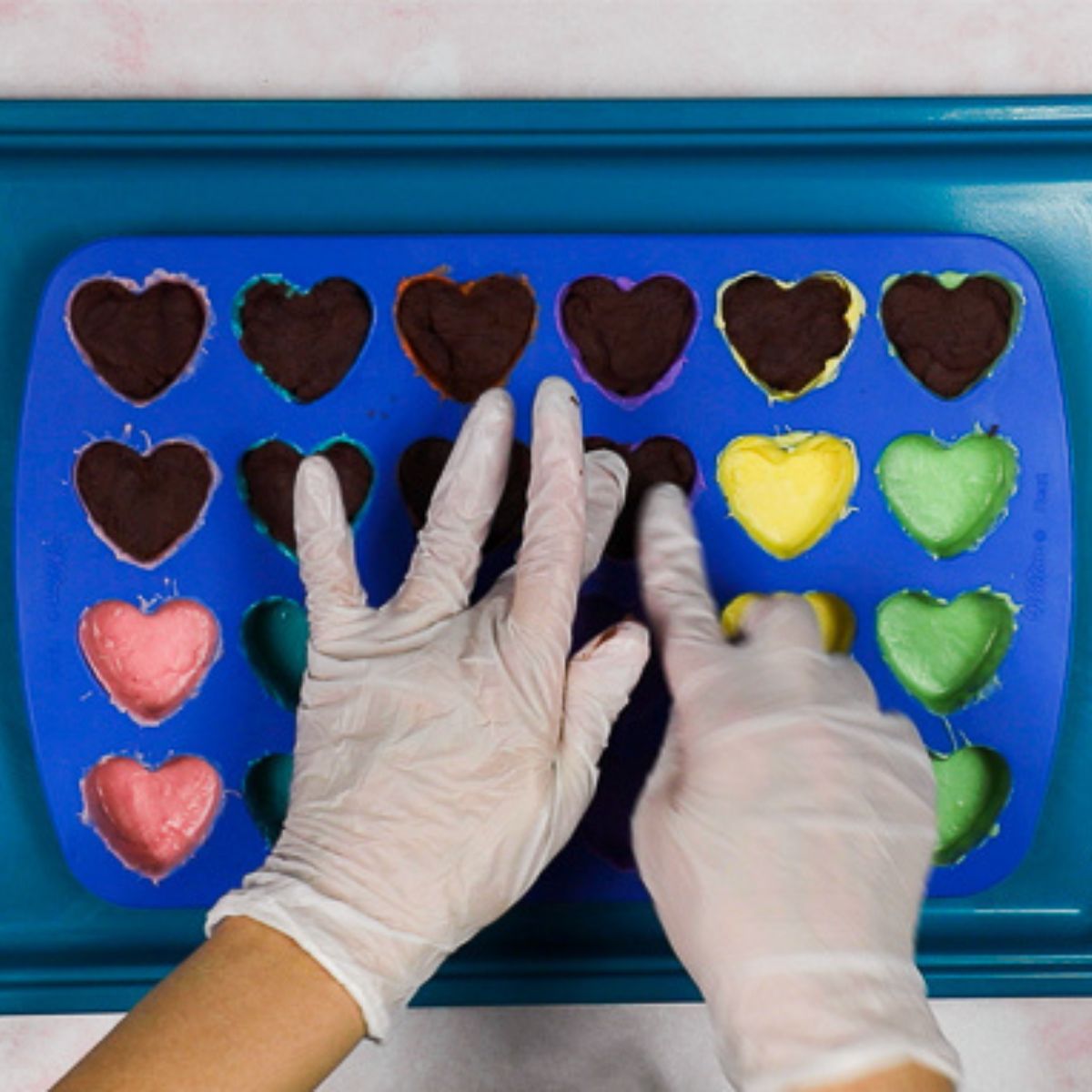 pressing cake filling into heart shaped silicone mold cavities.