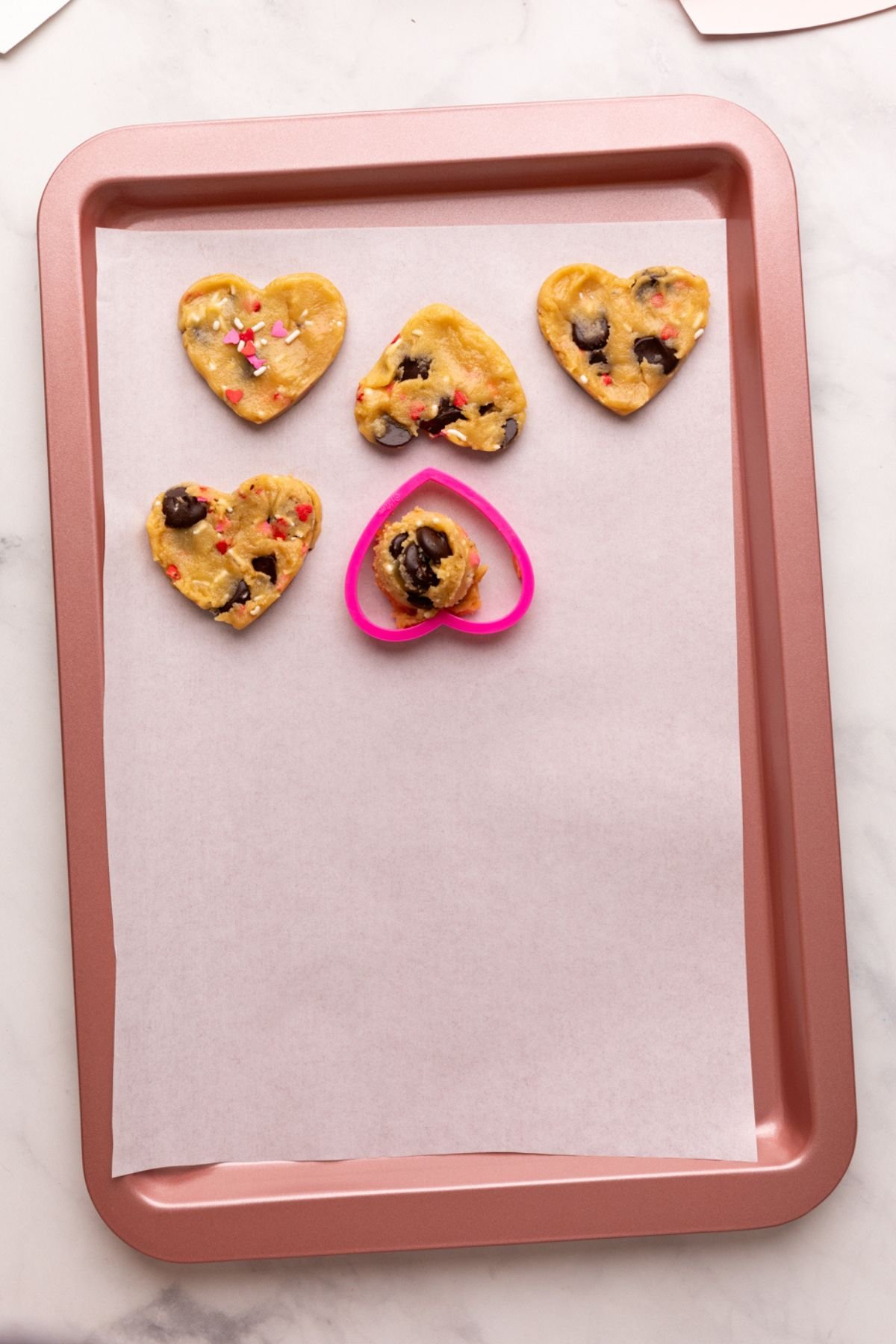 using a cookie cutter to shape chocolate chip cookies into hearts.