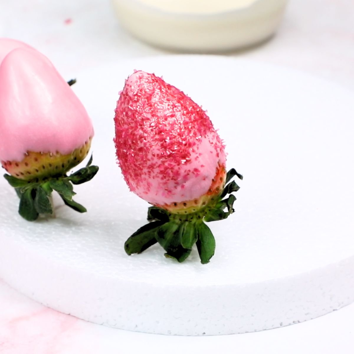 pink edible glitter on a pink dipped strawberry, drying upside down on a styrofoam board.