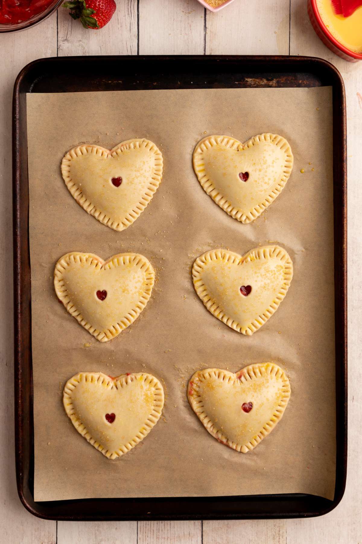 unbaked heart shaped hand pies on a baking sheet lined with brown parchment paper.