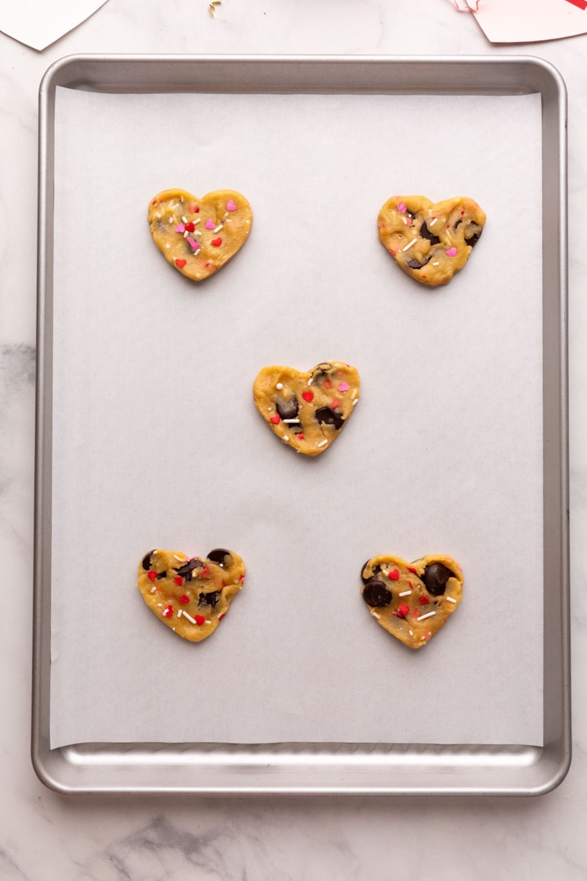 unbaked heart chocolate chip cookies on a parchment lined baking sheet.