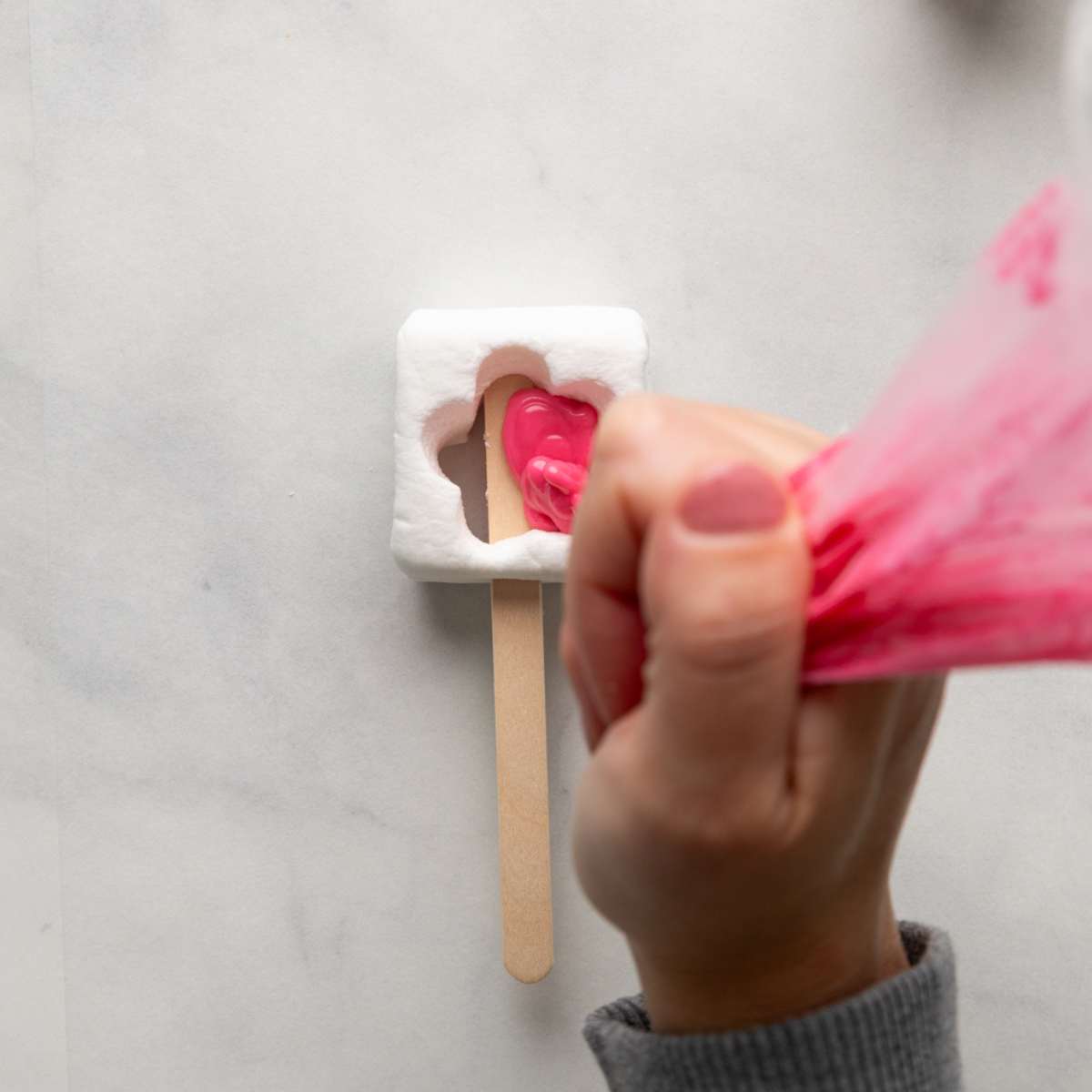 Adding pink chocolate to a marshmallow pop.
