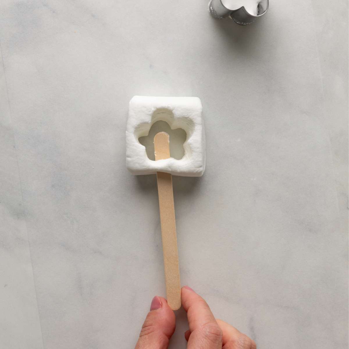 adding a popscicle stick to a marshmallow pop.