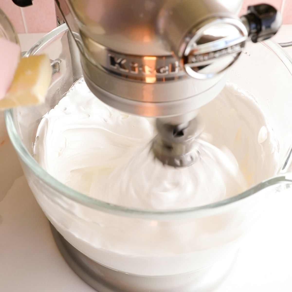 adding butter to a standing mixer with a glass bow of Italian meringue buttercream.