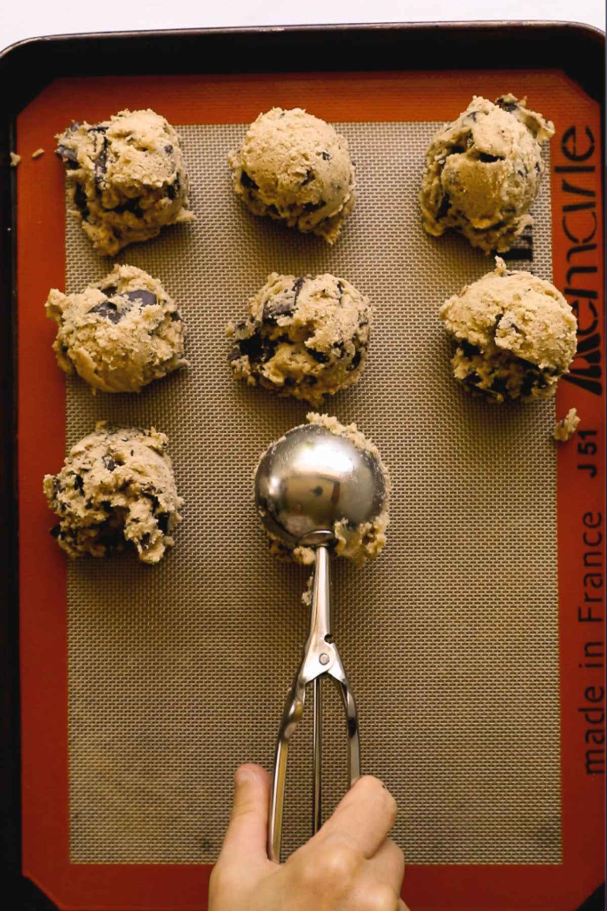scooping cokie dough balls on silicone baking mat-lined baking sheet before chilling.